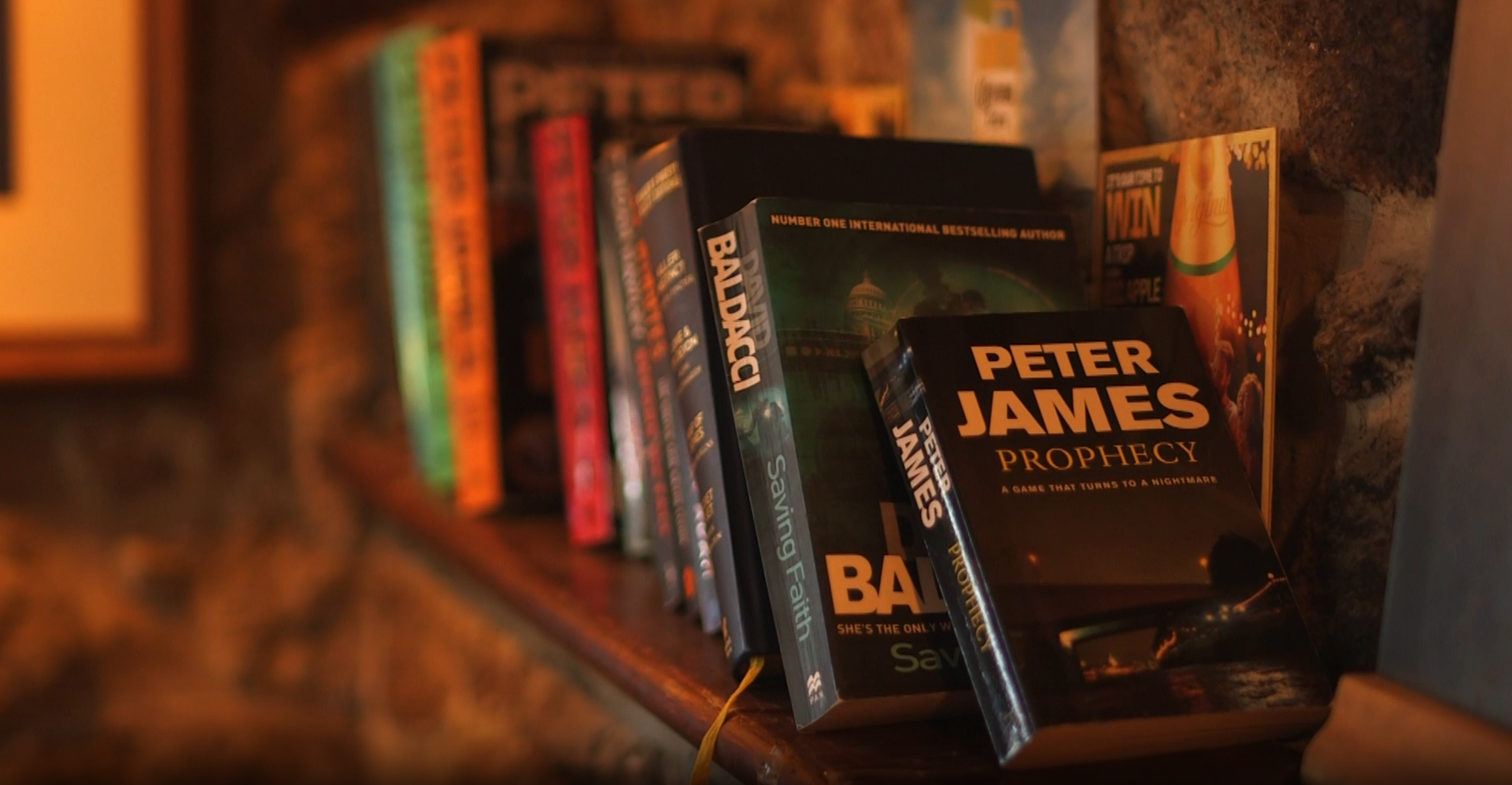 A row of worn paperbacks on a shelf in the bar, lit warm against stone